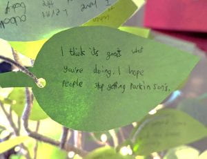 A green paper leaf with handwritten message reading: I think it's great what you're doing. I hope people stop getting Parkinson's.