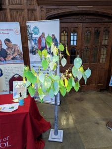 A model of a tree with green paper leaves on which people have hand-written messages about the CHIEF-PD study on Parkinson's.